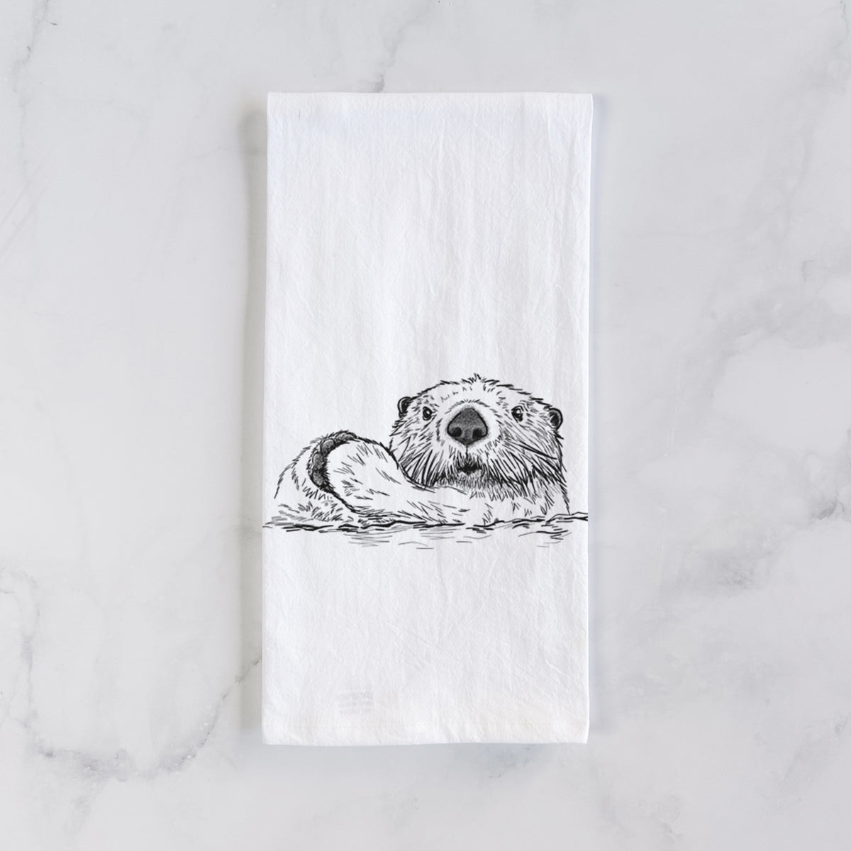 White cotton tea towel laid flat on marble, printed with a black ink illustration of a northern river otter peeking out of the water.