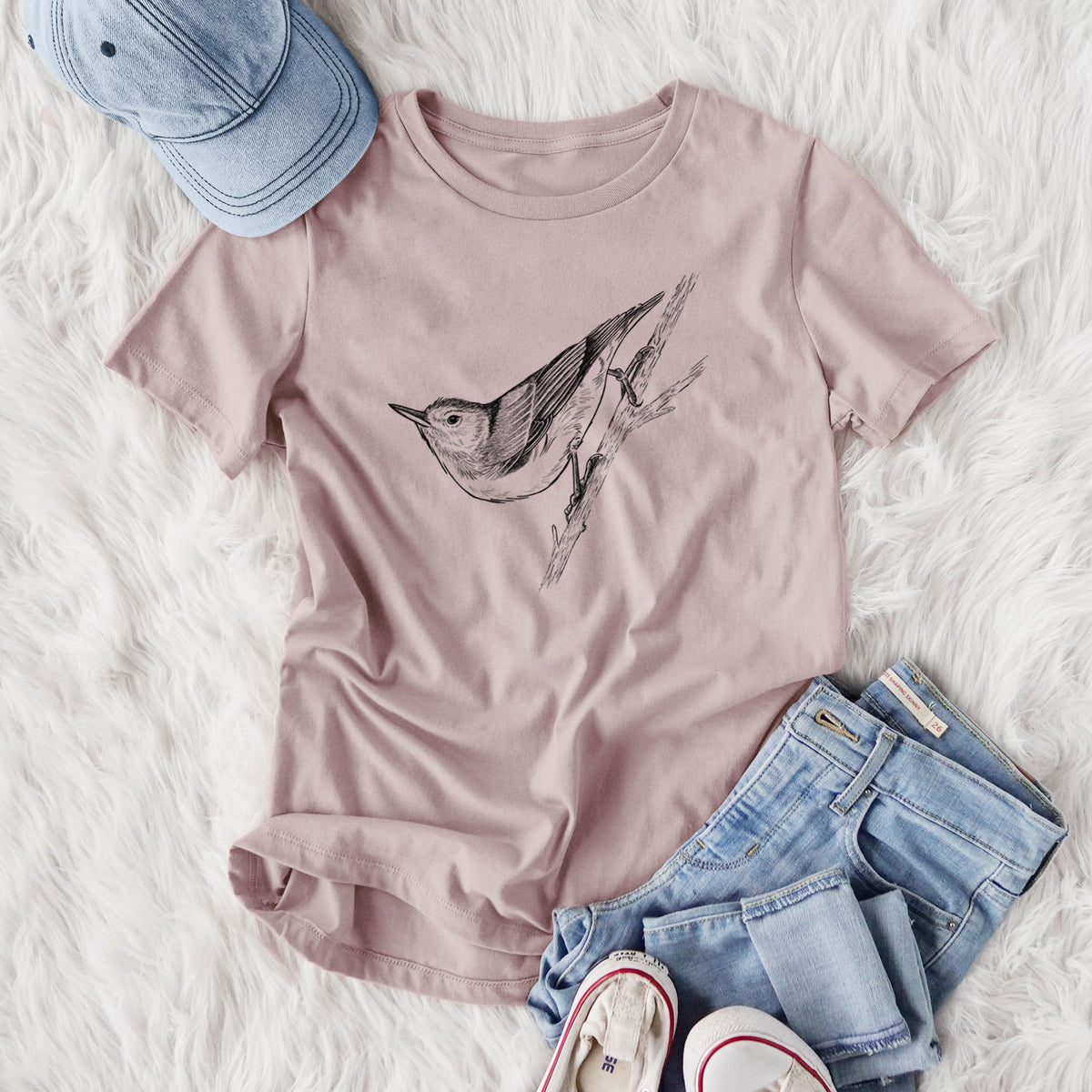 Women's relaxed fit cotton t-shirt printed with a detailed black ink sketch of a nuthatch clinging to a branch, styled flat on a white faux fur rug with jeans.