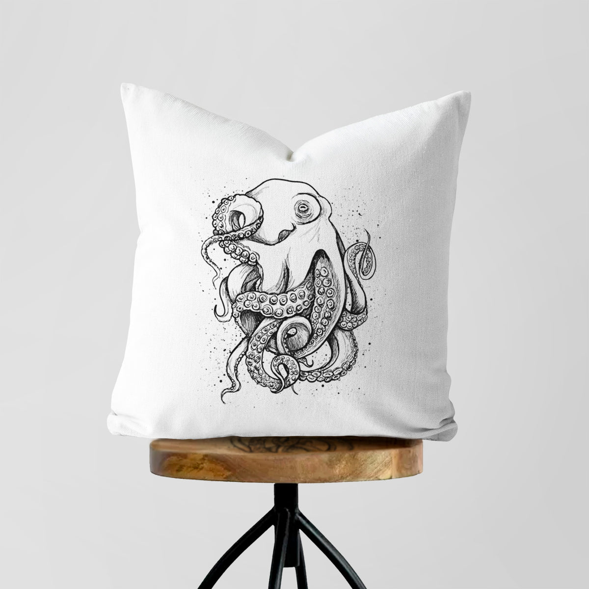 White pillow cover printed with a detailed black ink illustration of a common octopus with curling tentacles, on a wooden stool.
