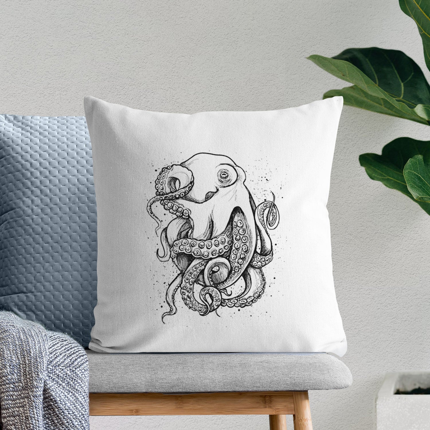 White pillow cover printed with a detailed black ink illustration of a common octopus with curling tentacles, on a bench beside plants.