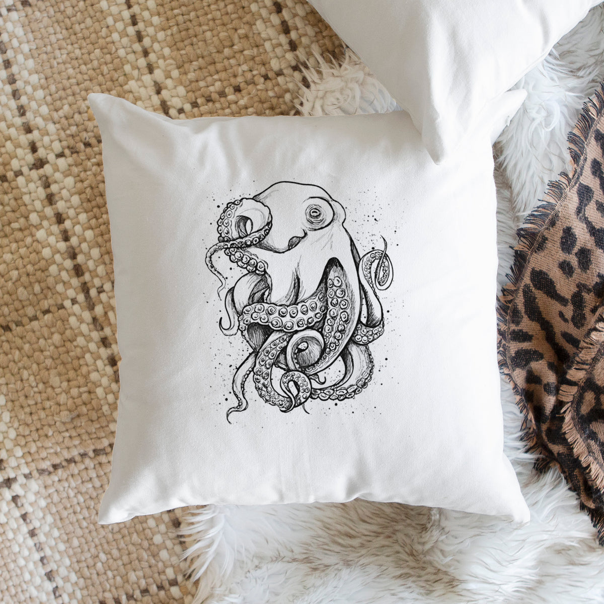 White pillow cover printed with a detailed black ink illustration of a common octopus with curling tentacles, on a woven chair.