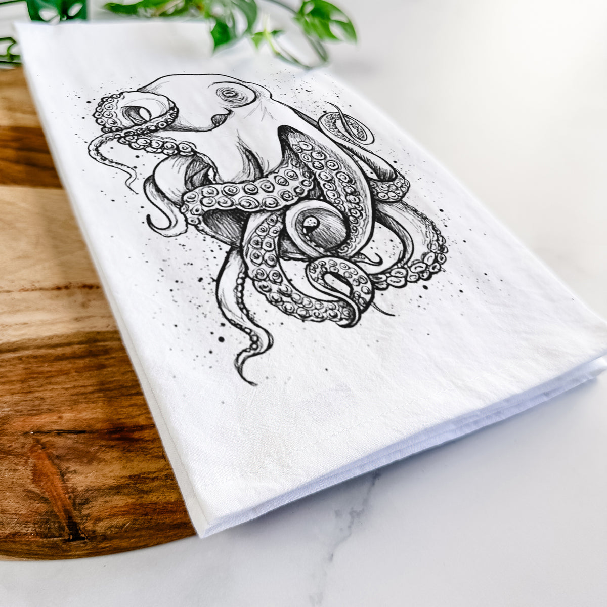 Close-up of a folded white tea towel on a wooden board, showing a detailed black ink illustration of a common octopus with curling tentacles.