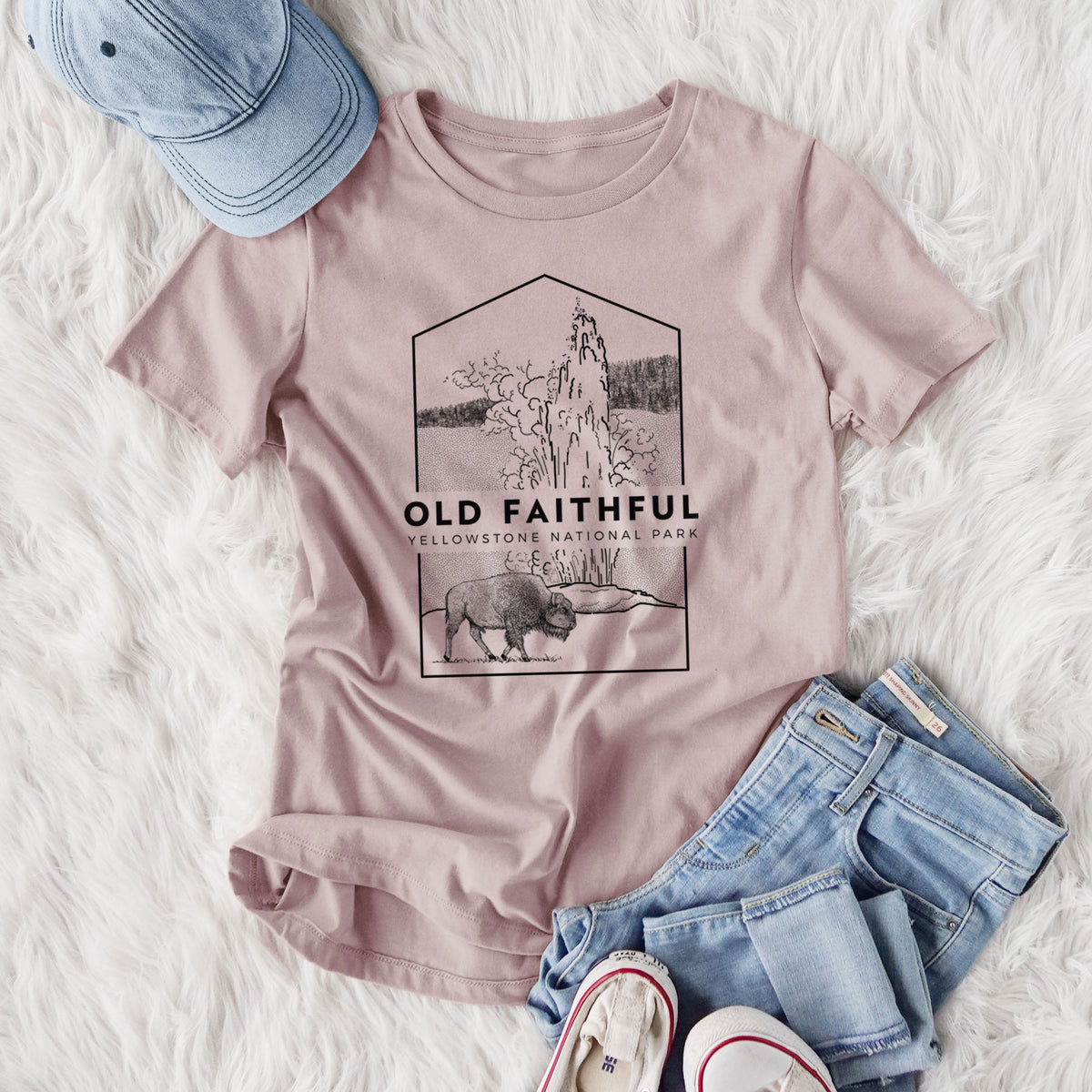 Women's relaxed fit cotton t-shirt printed with a black line art badge of the Old Faithful geyser erupting with a bison nearby, with the words Old Faithful, Yellowstone National Park, styled flat on a white faux fur rug with jeans.