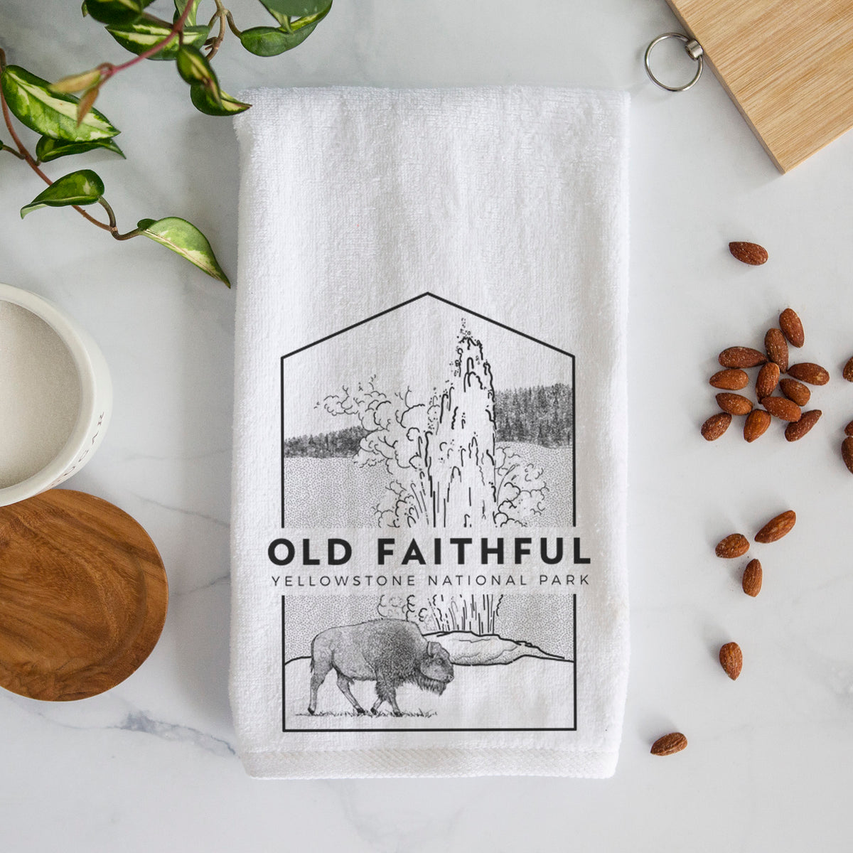 White hand towel printed with a black line art badge of the Old Faithful geyser erupting with a bison nearby, with the words Old Faithful, Yellowstone National Park.