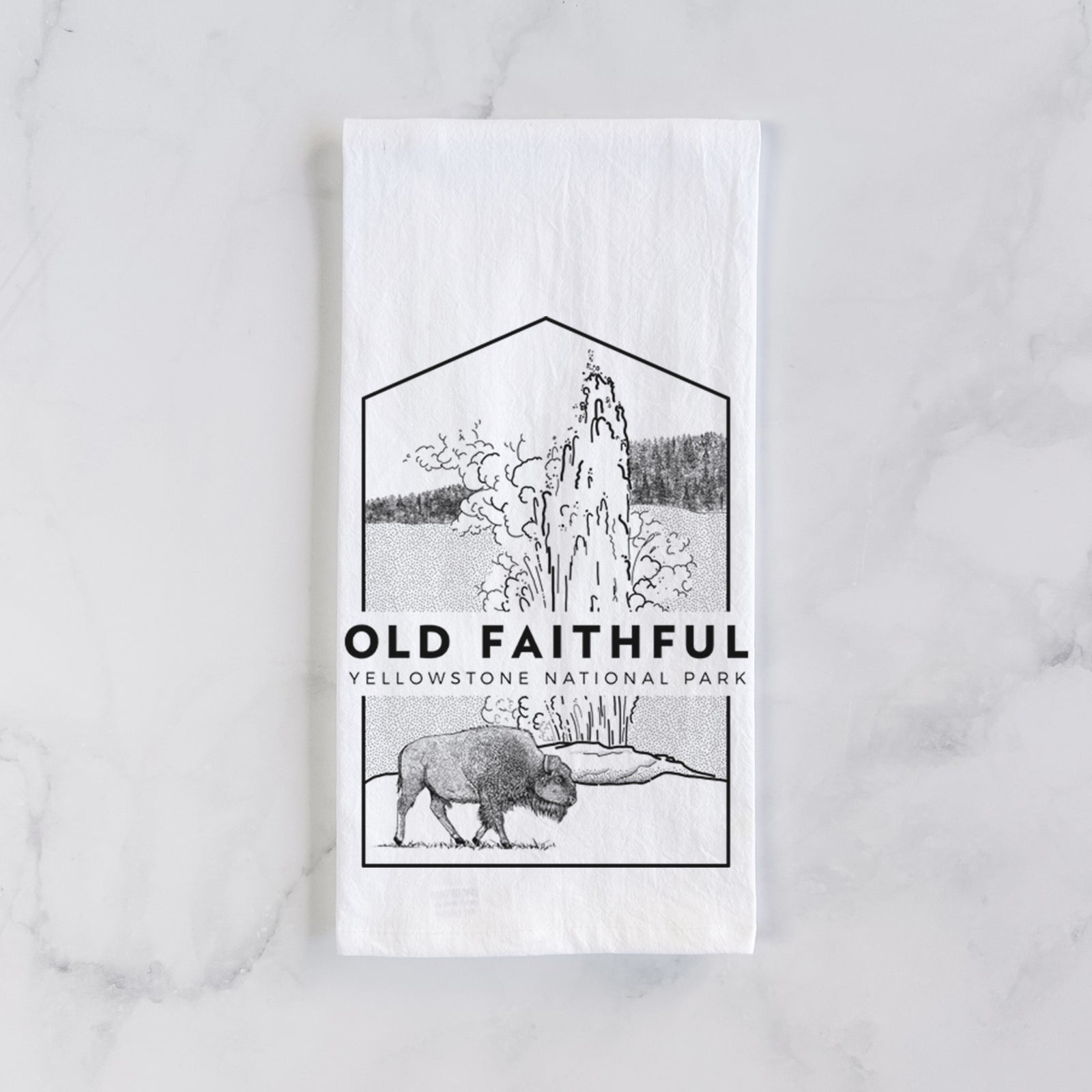 White cotton tea towel printed with a black line art badge of the Old Faithful geyser erupting with a bison nearby, with the words Old Faithful, Yellowstone National Park, on a marble counter beside a round wooden cutting board and greenery.