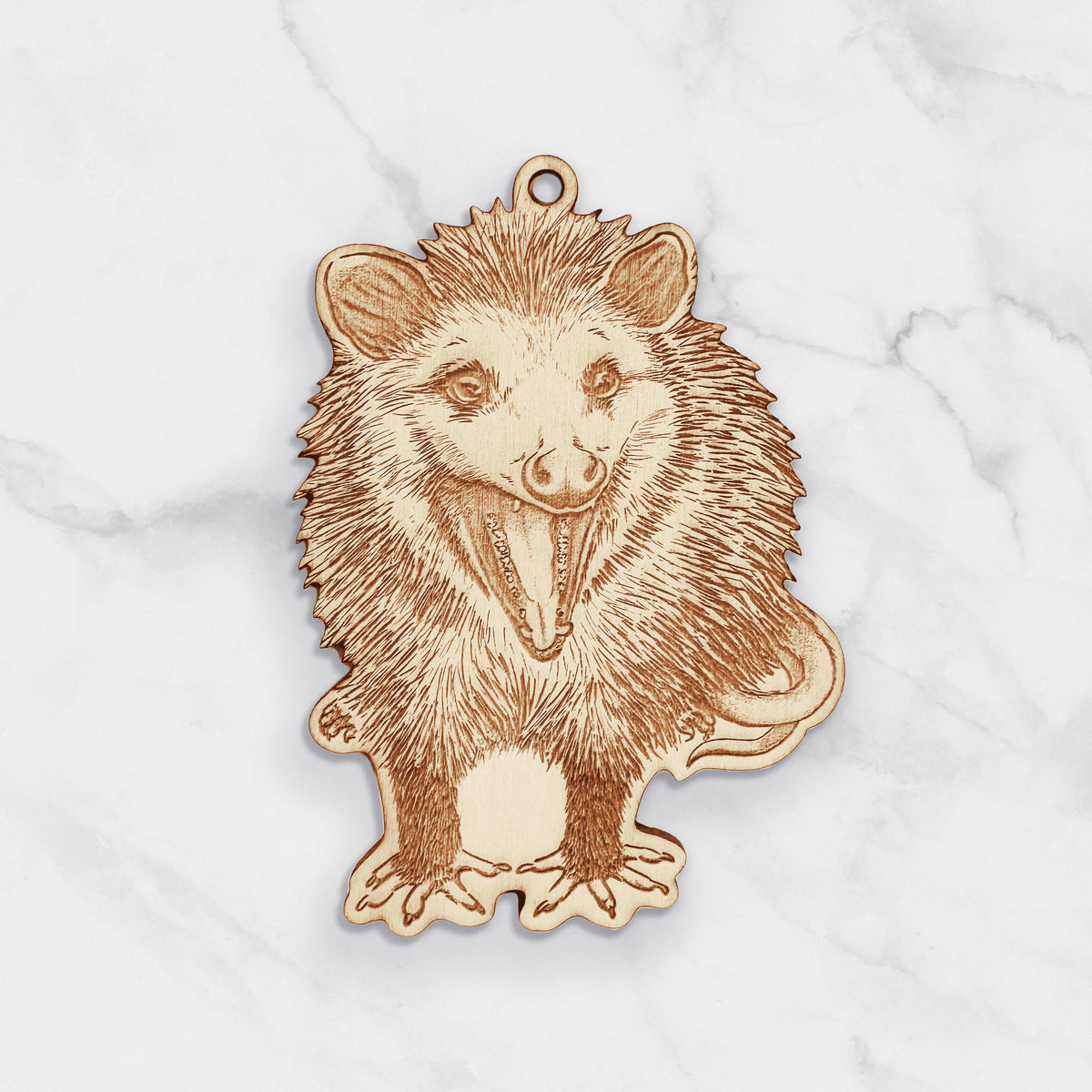 Wooden ornament featuring a detailed engraving of a hissing opossum standing and facing forward, on a marble surface.