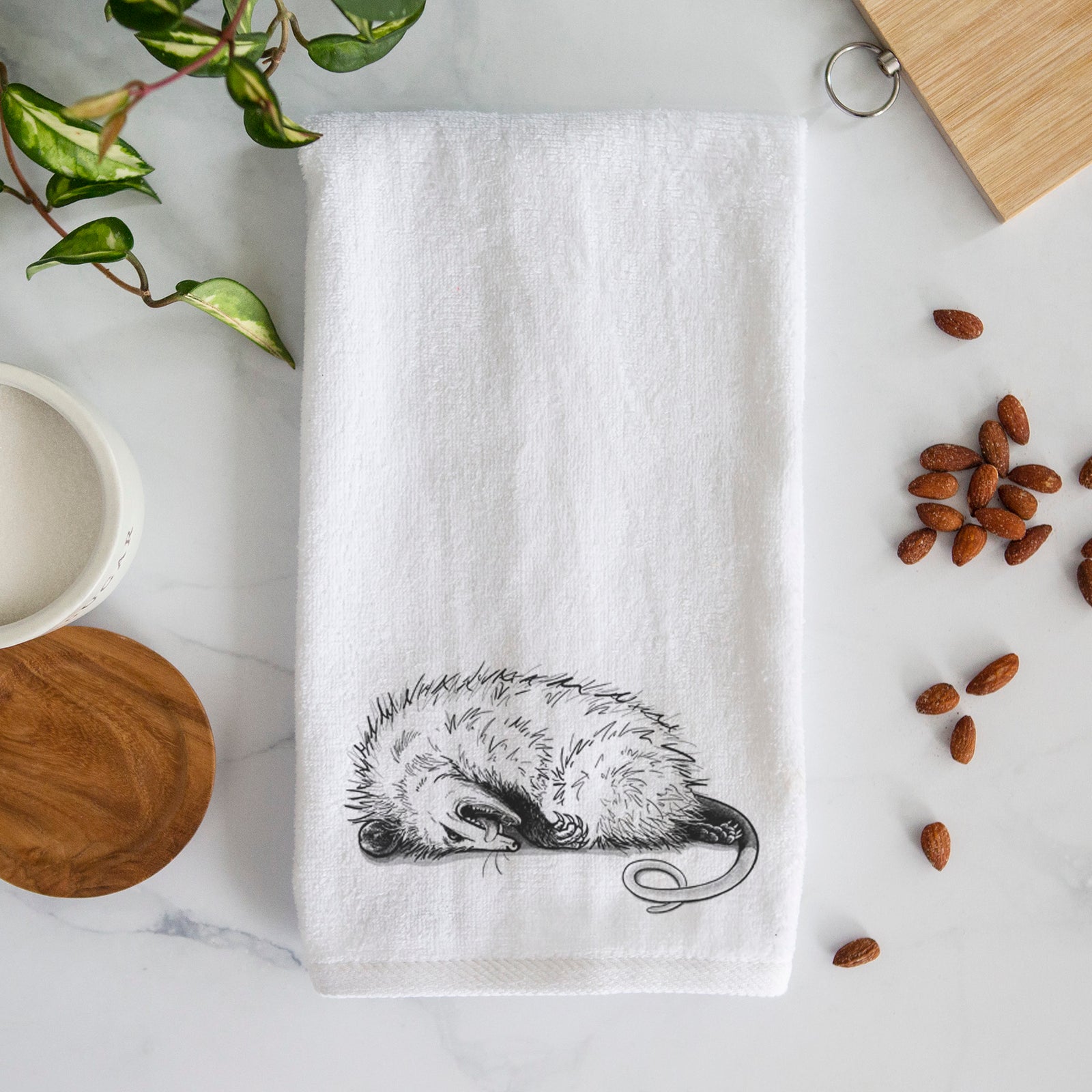 White hand towel printed with a black ink illustration of an opossum lying on its side playing dead.