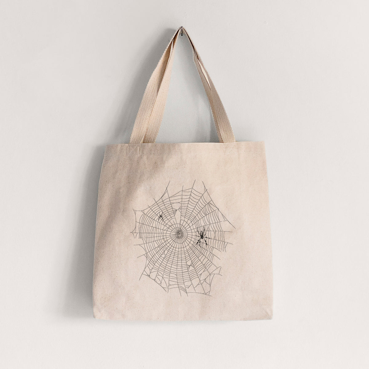 Natural canvas tote bag printed with a black ink line drawing of an orb weaver spider in the center of its web.
