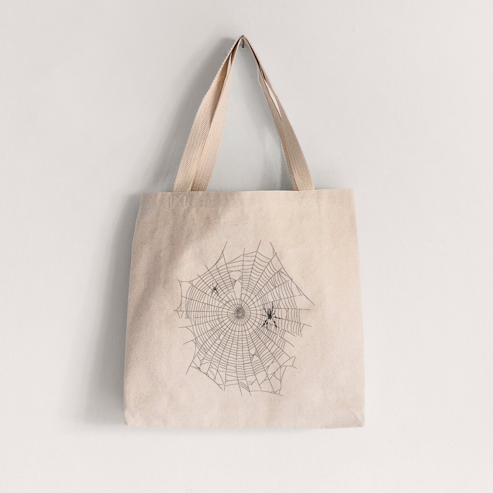 Natural canvas tote bag printed with a black ink line drawing of an orb weaver spider in the center of its web.