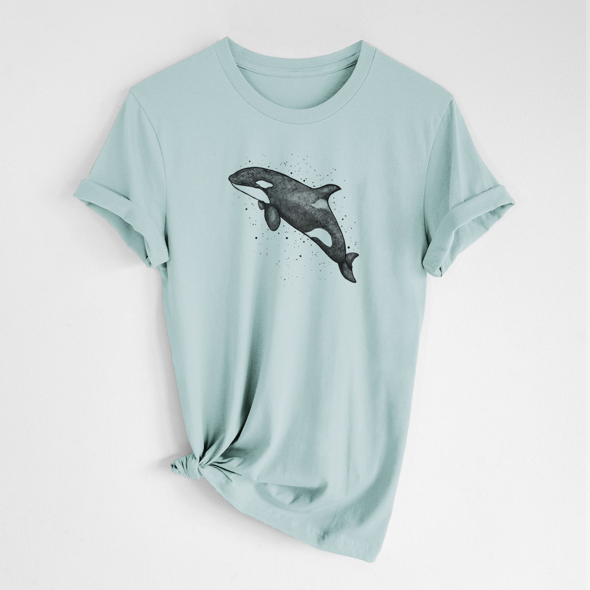 Dusty blue lightweight cotton t-shirt laid flat with the sleeves rolled, printed with a black ink illustration of an orca leaping, with ink splatters.