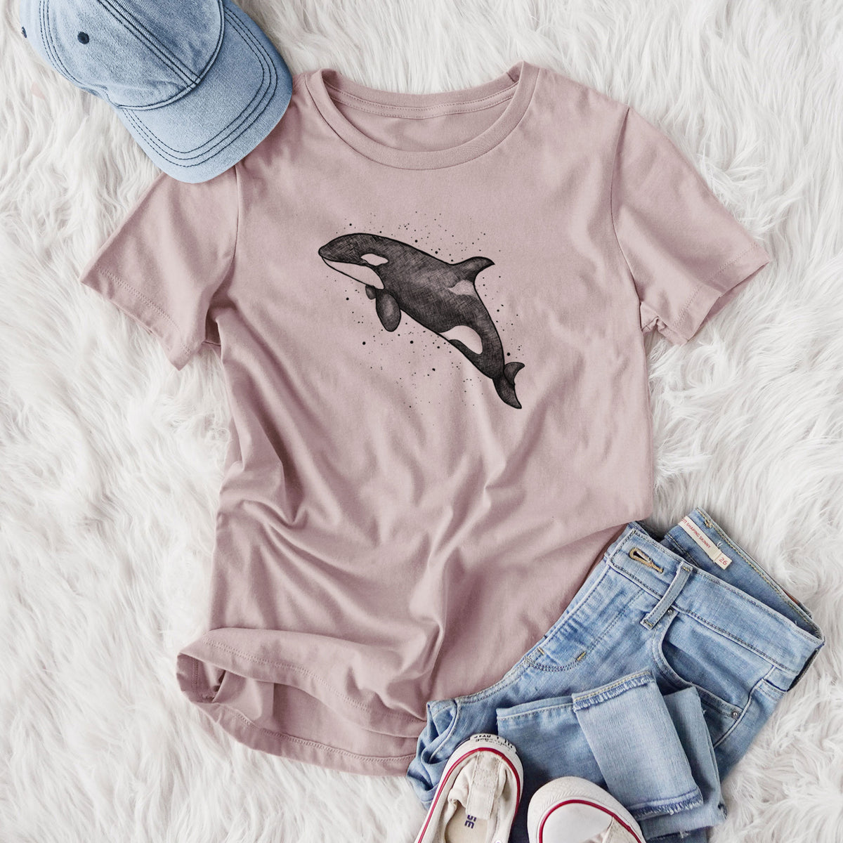 Women's relaxed fit cotton t-shirt printed with a black ink illustration of an orca leaping, with ink splatters, styled flat on a white faux fur rug with jeans.