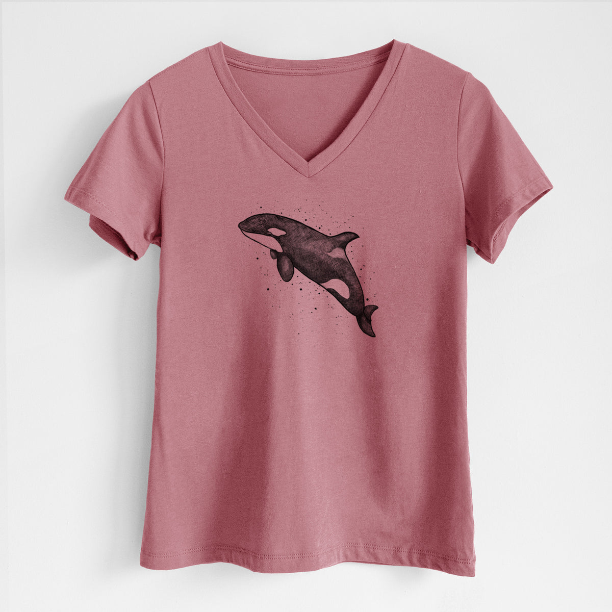 Mauve pink women's relaxed fit cotton V-neck t-shirt laid flat, printed with a black ink illustration of an orca leaping, with ink splatters.