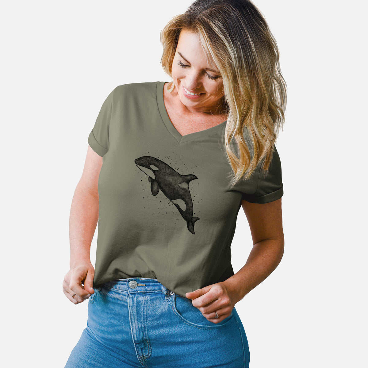 Woman wearing a military green women's relaxed fit cotton V-neck t-shirt printed with a black ink illustration of an orca leaping, with ink splatters.