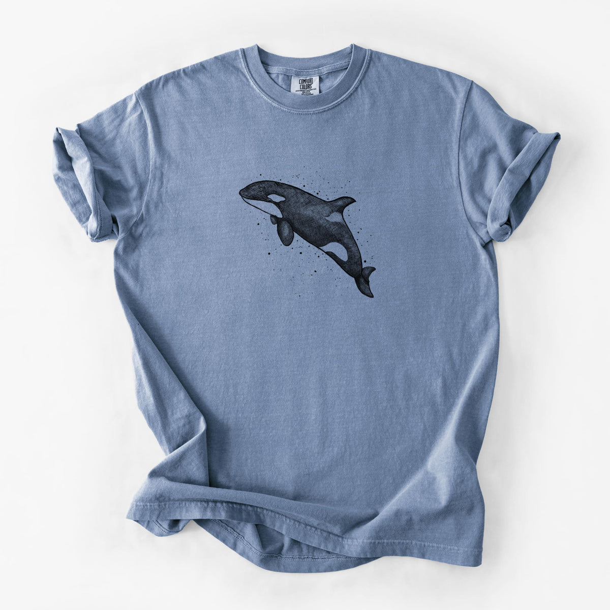 Blue jean Comfort Colors t-shirt laid flat, printed with a black ink illustration of an orca leaping, with ink splatters.