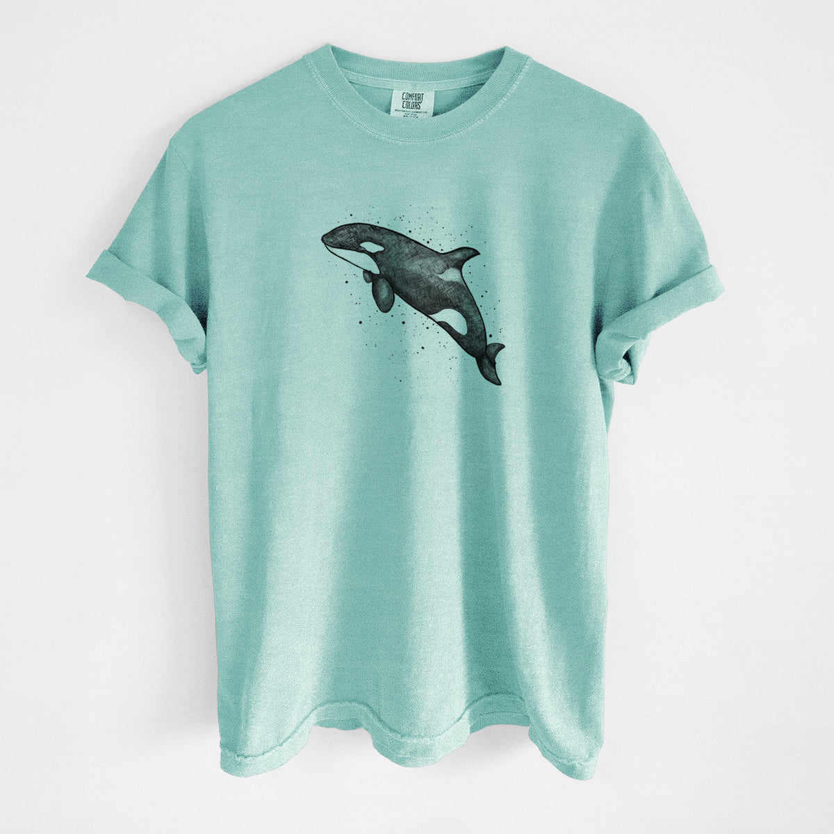 Chalky mint Comfort Colors t-shirt laid flat, printed with a black ink illustration of an orca leaping, with ink splatters.