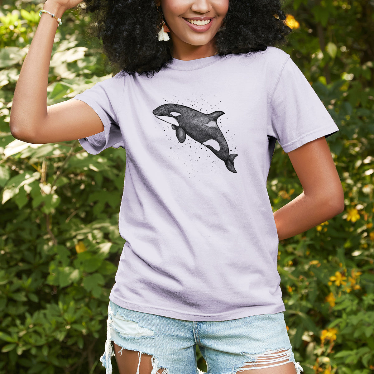 Woman wearing a Comfort Colors t-shirt printed with a black ink illustration of an orca leaping, with ink splatters, outdoors.