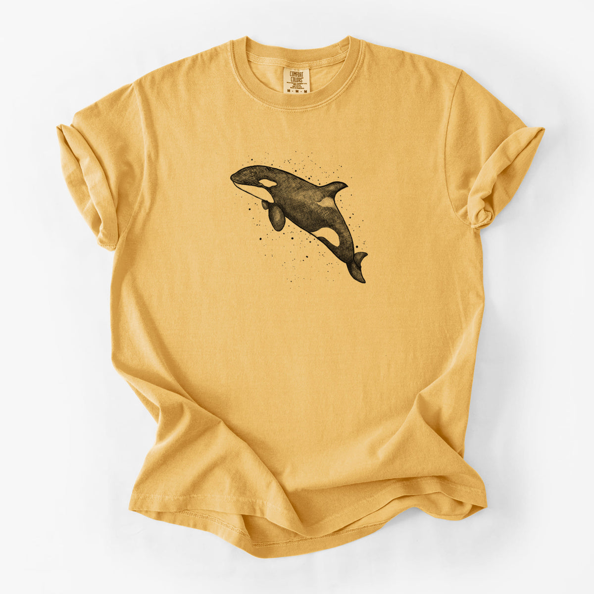 Golden wheat yellow Comfort Colors t-shirt laid flat, printed with a black ink illustration of an orca leaping, with ink splatters.