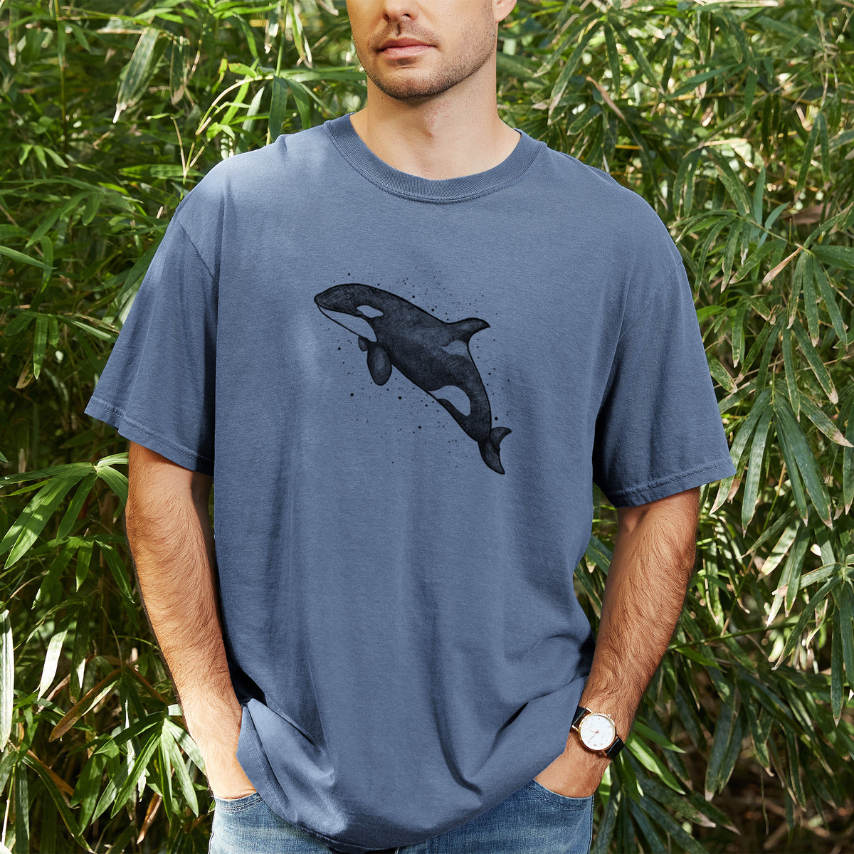 Man wearing a Comfort Colors t-shirt printed with a black ink illustration of an orca leaping, with ink splatters, outdoors.