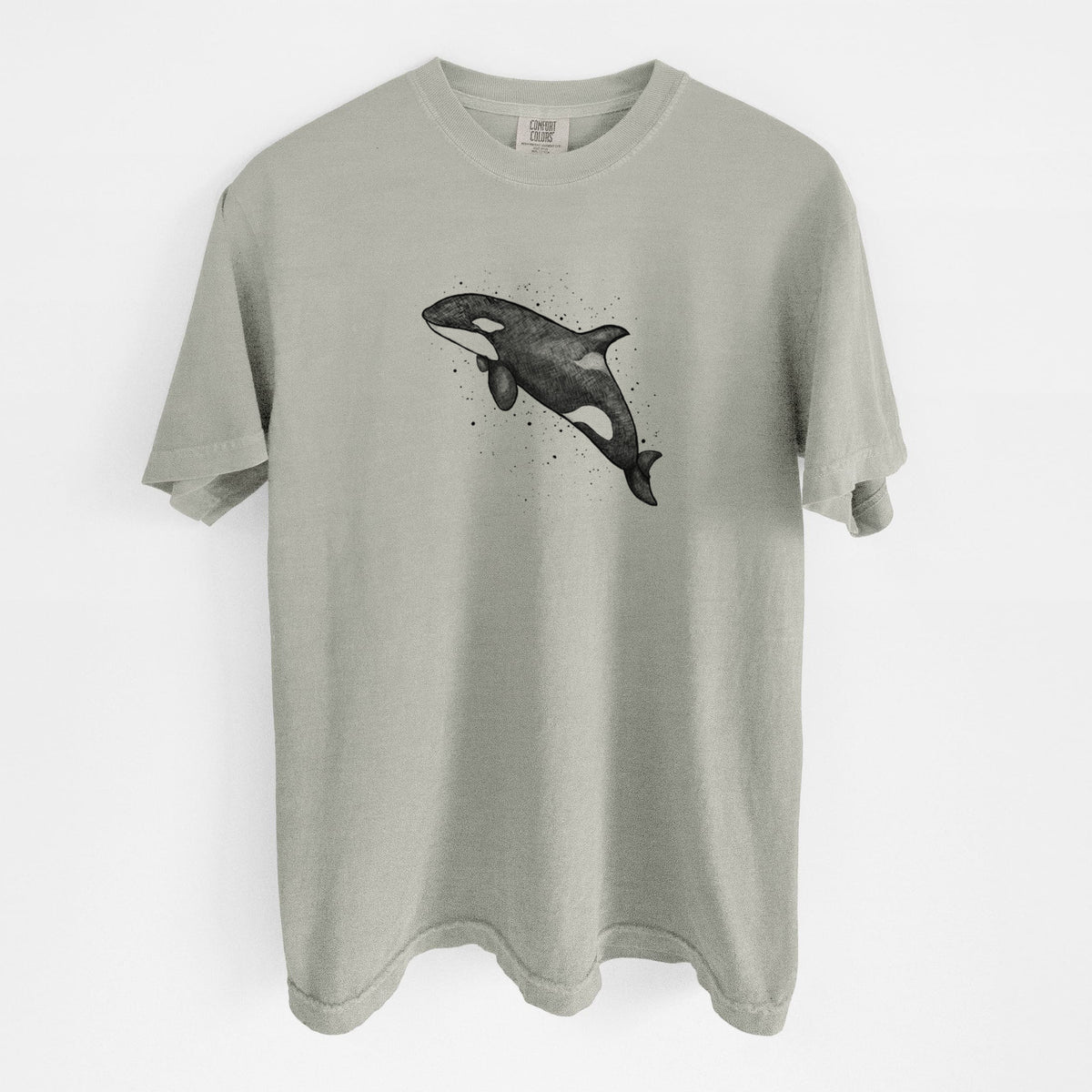Sandstone beige Comfort Colors t-shirt laid flat, printed with a black ink illustration of an orca leaping, with ink splatters.