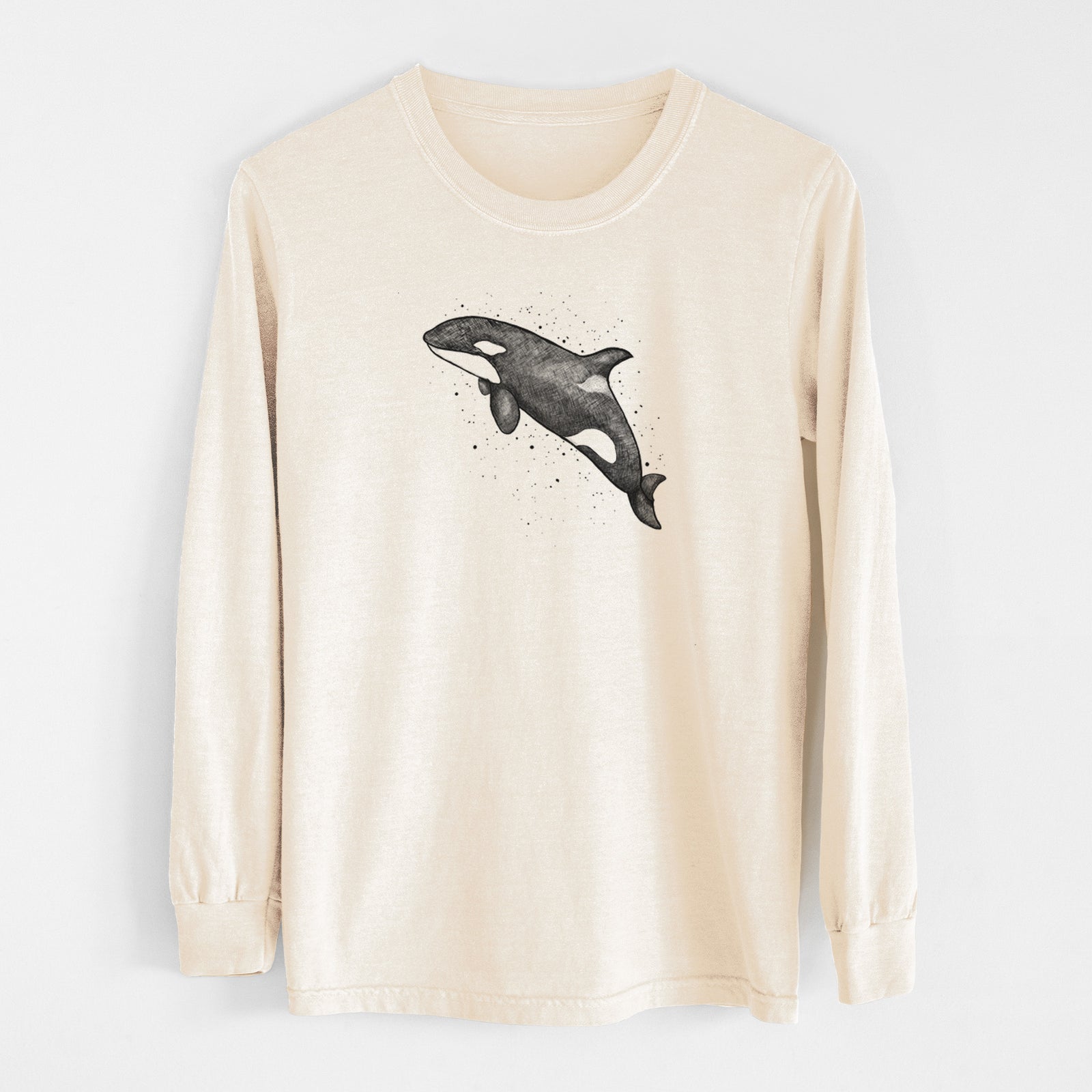 Ivory Comfort Colors long sleeve shirt laid flat, printed with a black ink illustration of an orca leaping, with ink splatters.