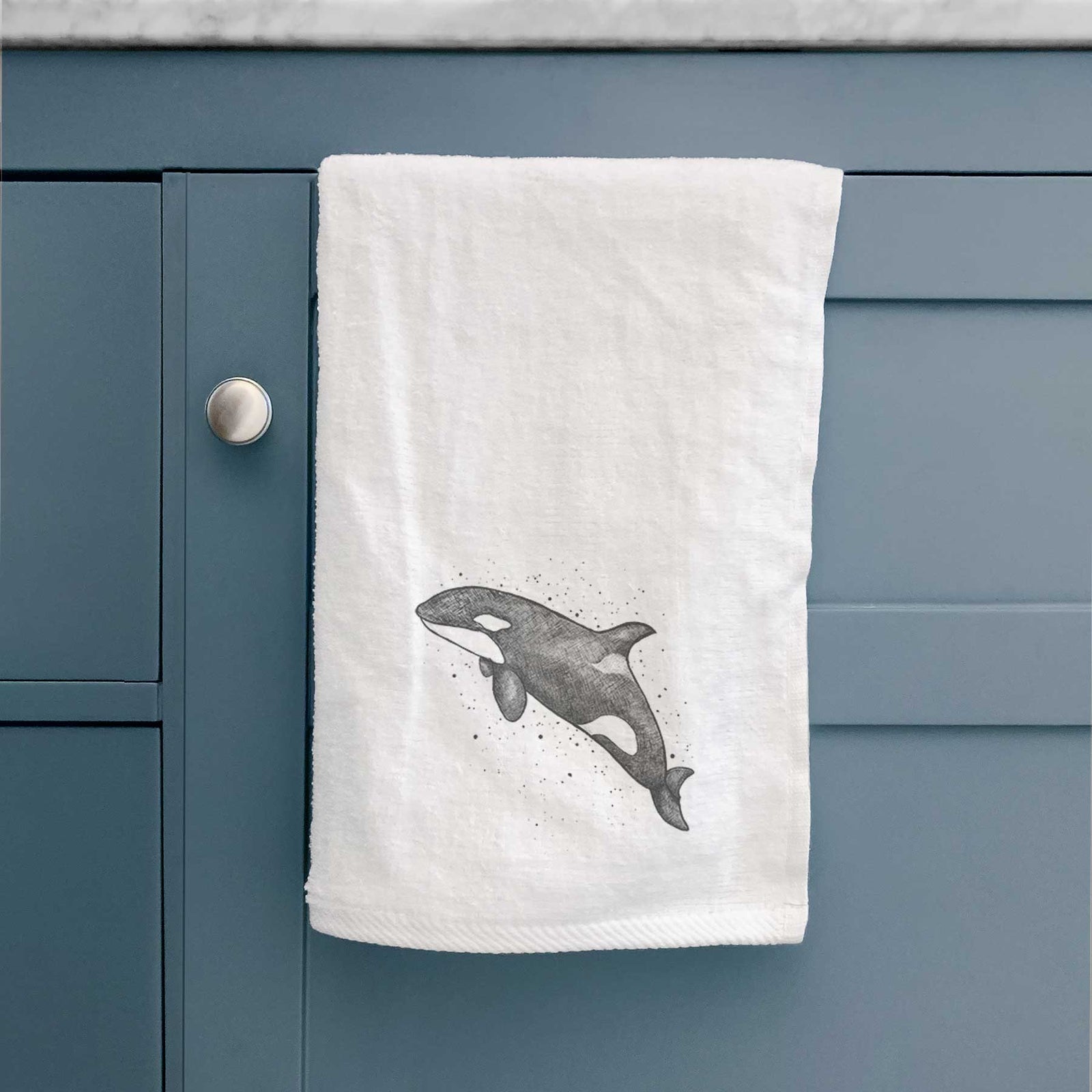 White hand towel printed with a black ink illustration of an orca leaping, with ink splatters.