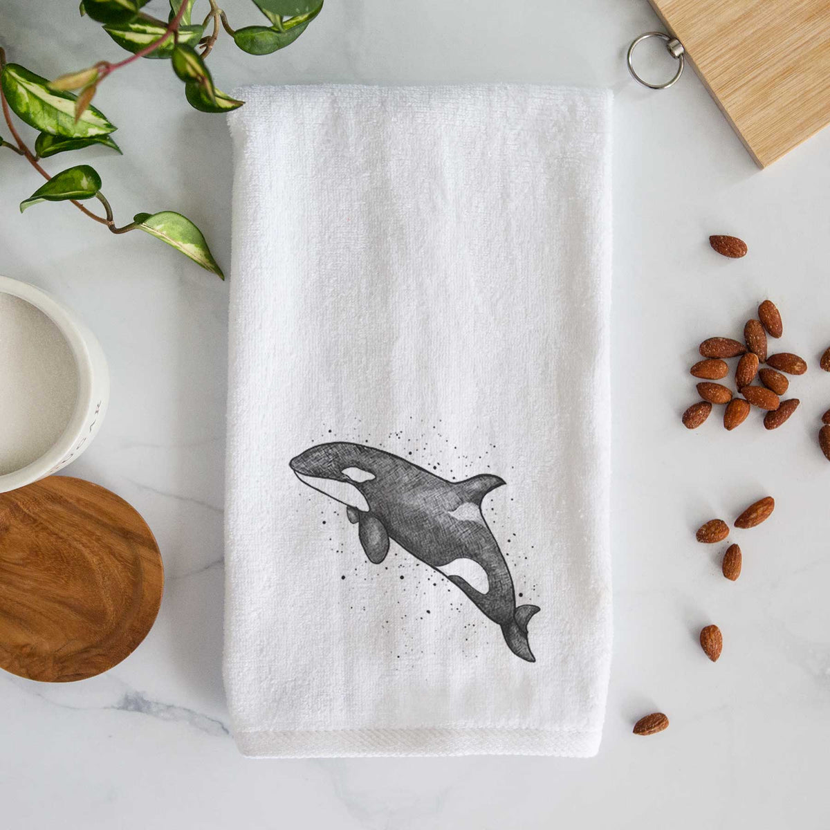 White hand towel printed with a black ink illustration of an orca leaping, with ink splatters.