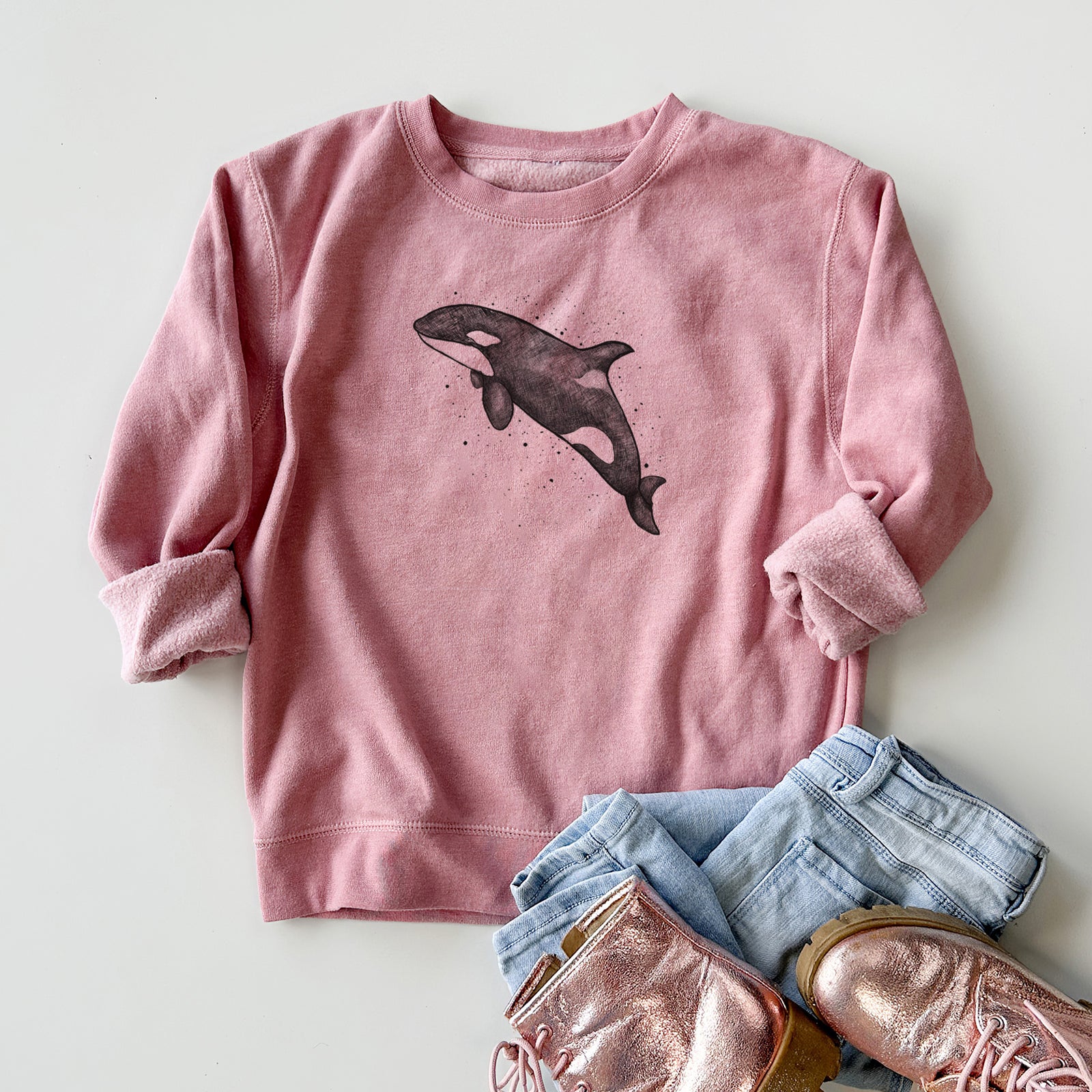 Boy wearing a youth crewneck sweatshirt printed with a black ink illustration of an orca leaping, with ink splatters, outdoors.