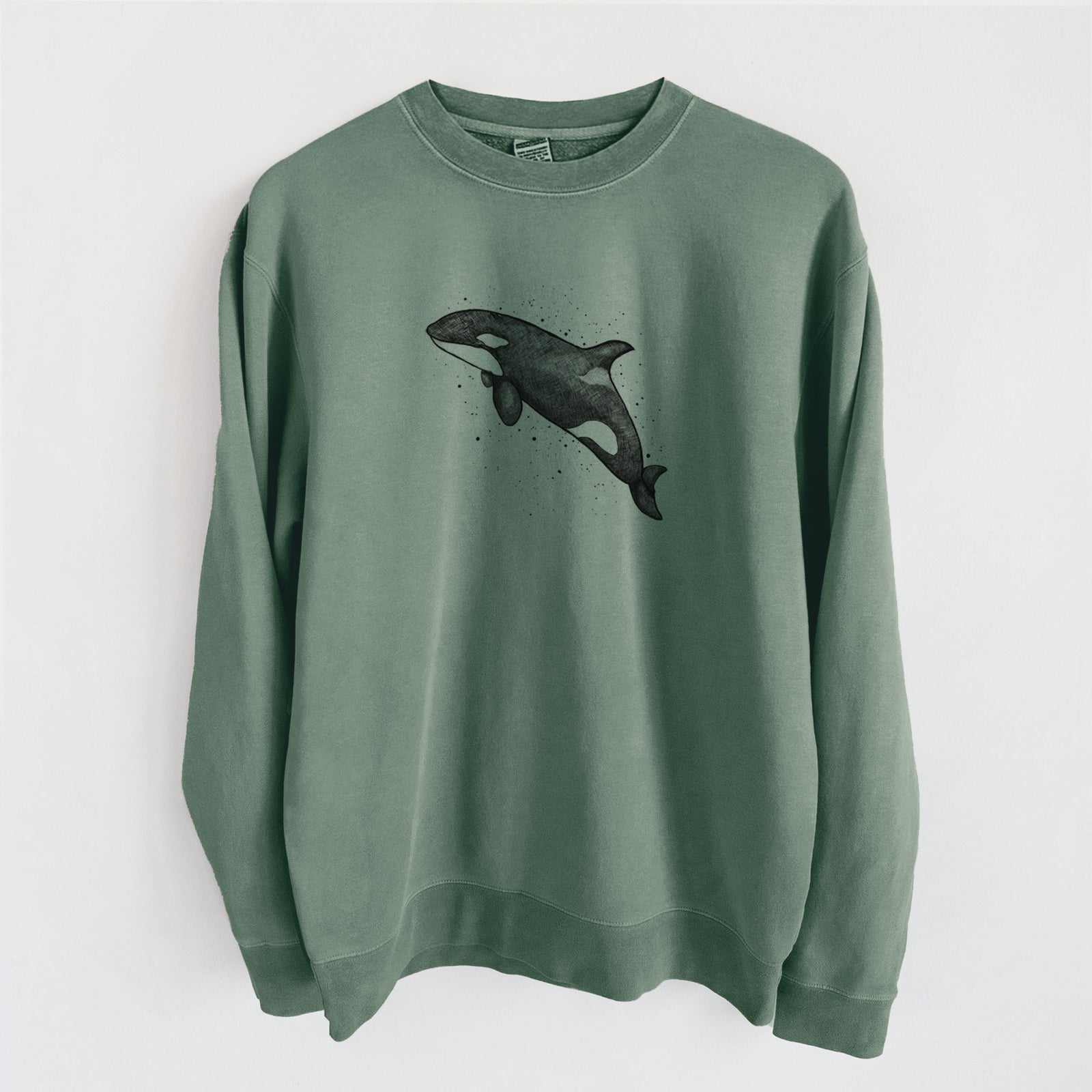 Alpine green pigment dyed crewneck sweatshirt laid flat, printed with a black ink illustration of an orca leaping, with ink splatters.