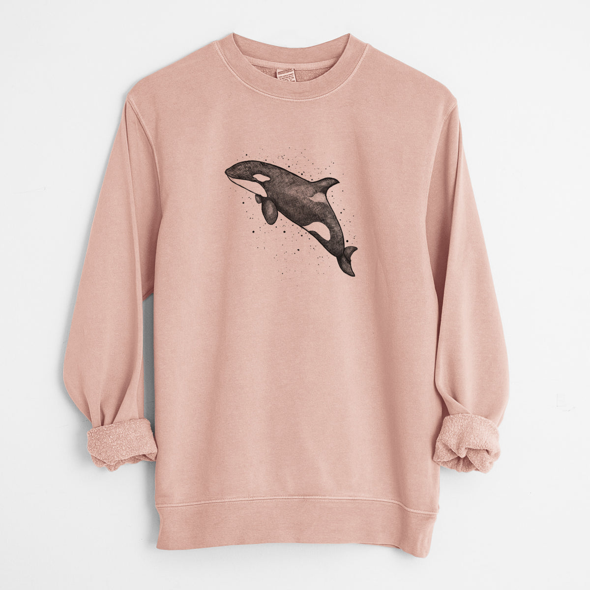 Dusty pink pigment dyed crewneck sweatshirt laid flat with the sleeves rolled, printed with a black ink illustration of an orca leaping, with ink splatters.