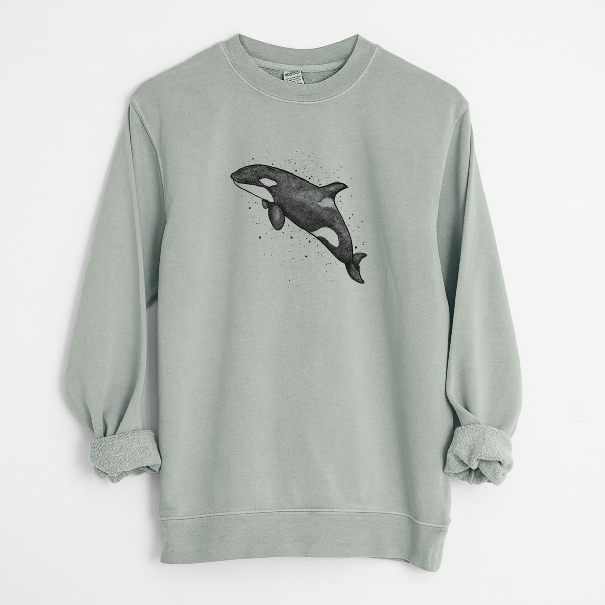 Sage green pigment dyed crewneck sweatshirt laid flat with the sleeves rolled, printed with a black ink illustration of an orca leaping, with ink splatters.