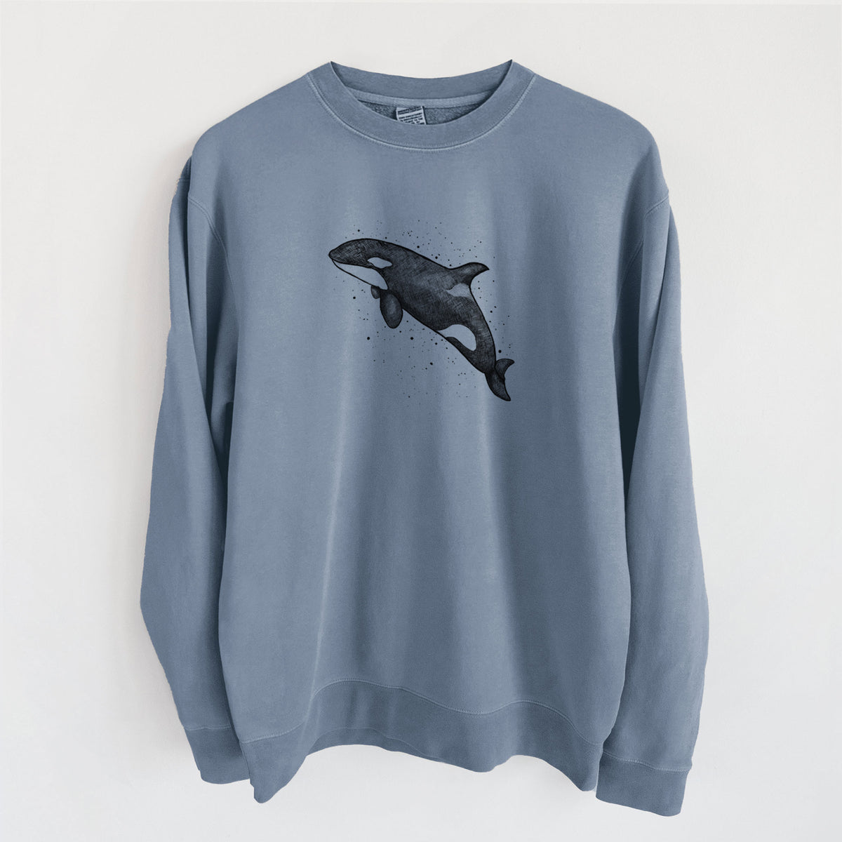Slate blue pigment dyed crewneck sweatshirt laid flat, printed with a black ink illustration of an orca leaping, with ink splatters.