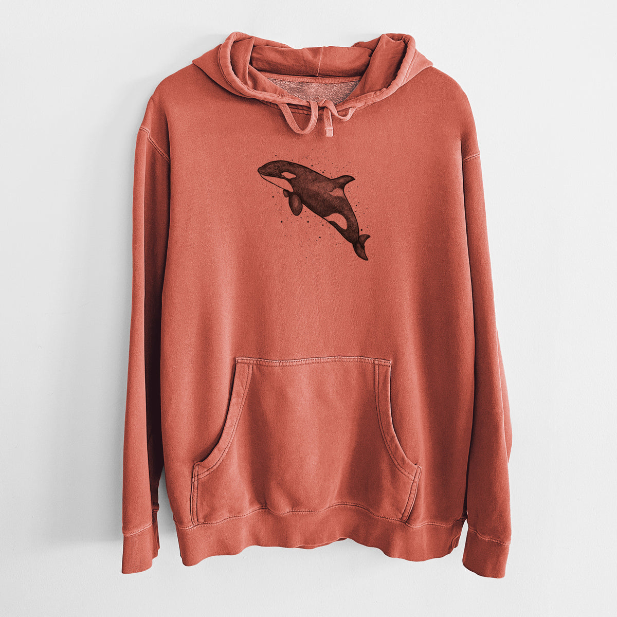 Amber orange pigment dyed hoodie laid flat, printed with a black ink illustration of an orca leaping, with ink splatters.