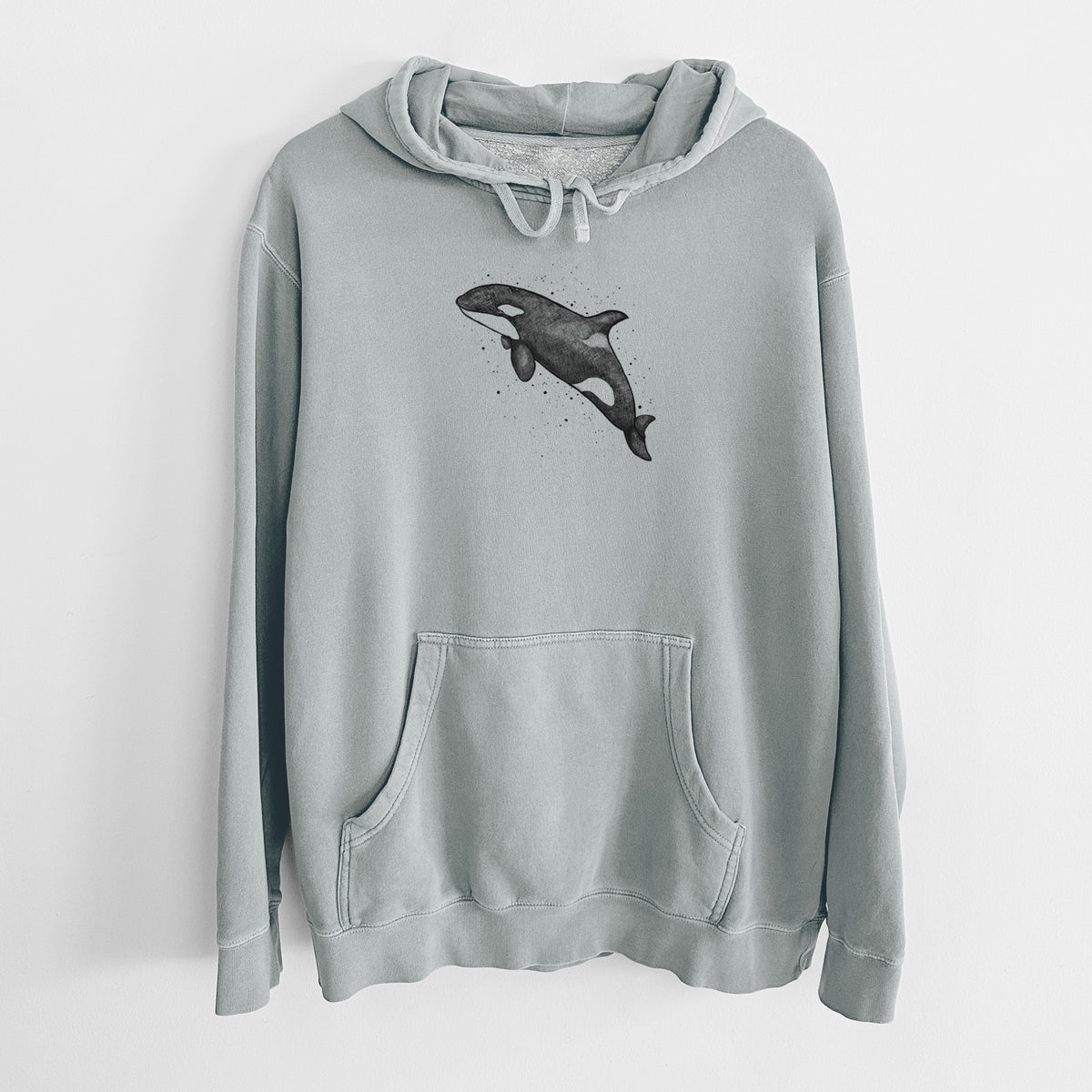 Sage green pigment dyed hoodie laid flat, printed with a black ink illustration of an orca leaping, with ink splatters.