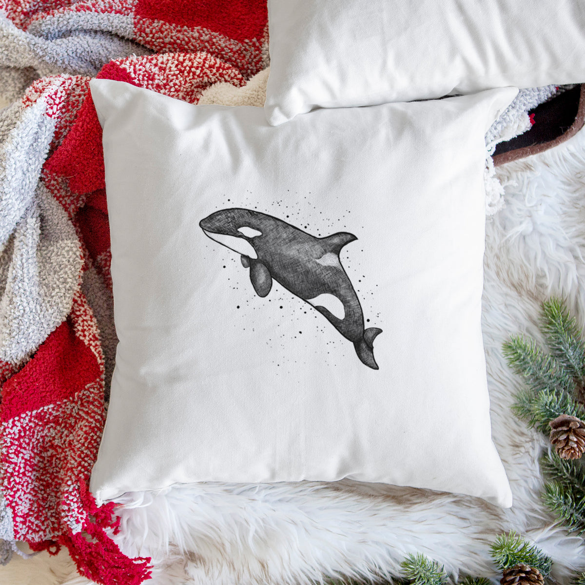 White pillow cover printed with a black ink illustration of an orca leaping, with ink splatters, on a woven chair.