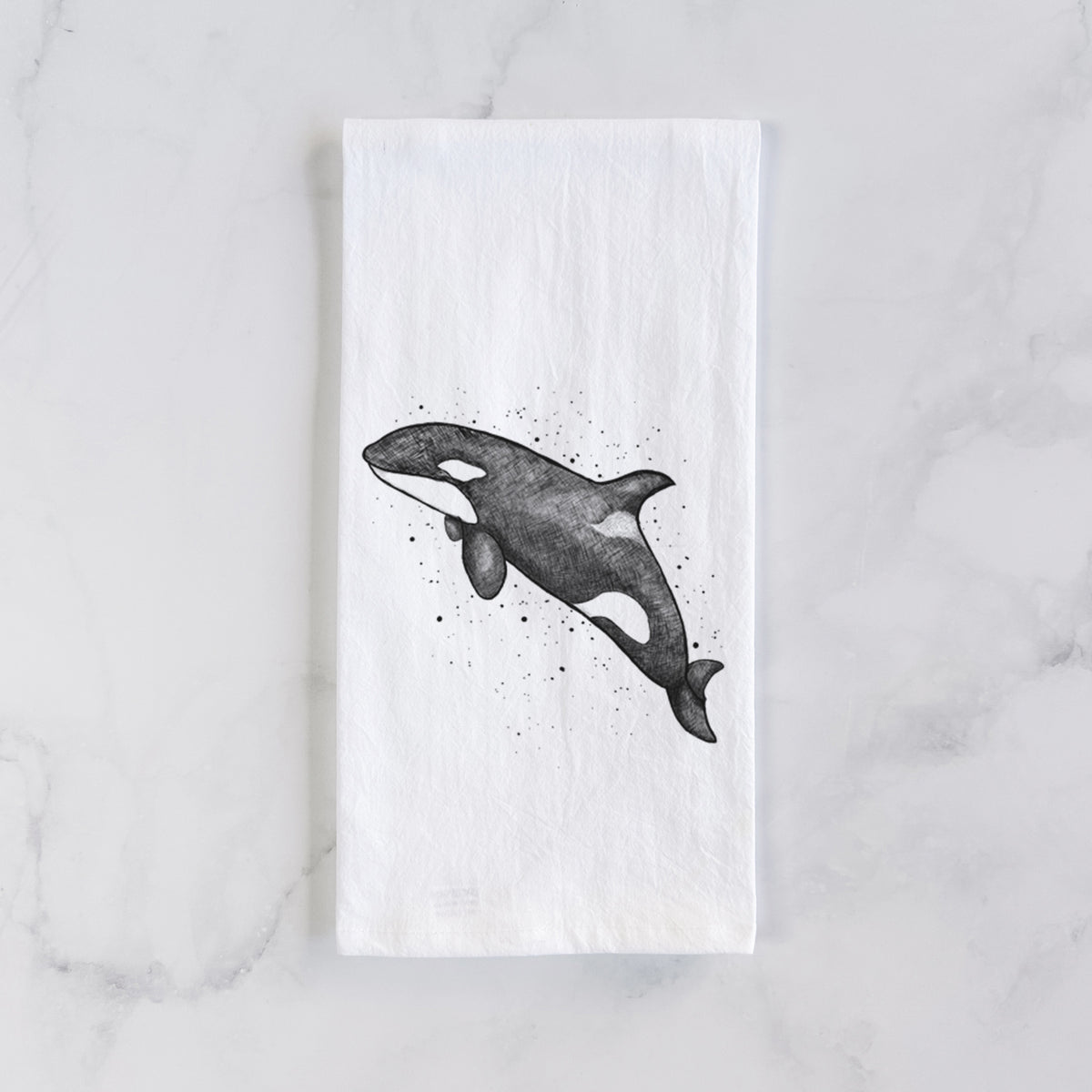White cotton tea towel laid flat on marble, printed with a black ink illustration of an orca leaping, with ink splatters.
