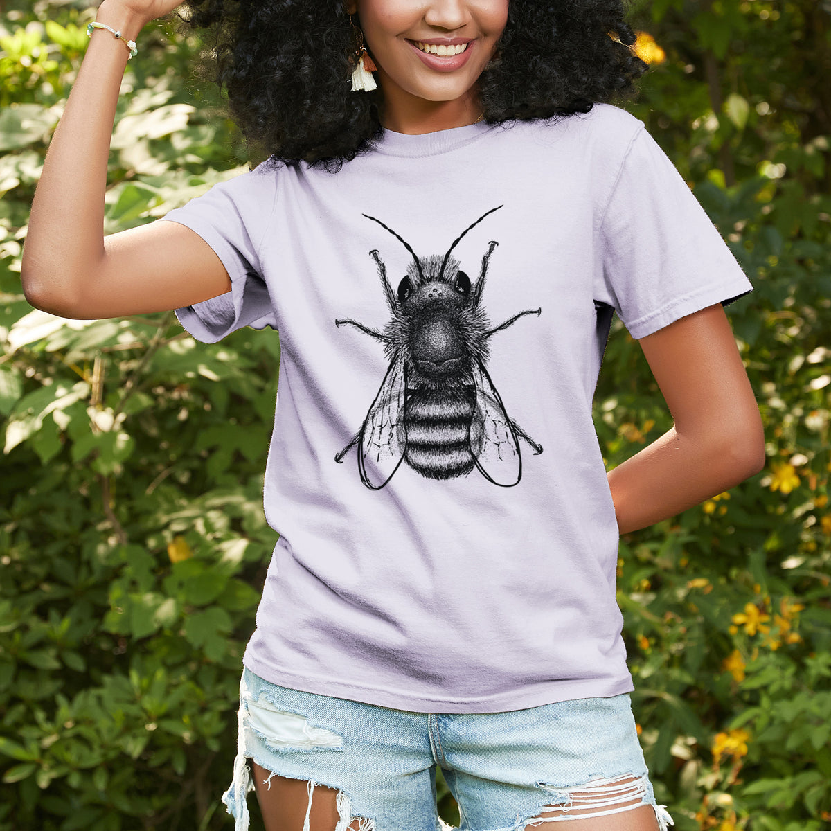Woman wearing a Comfort Colors t-shirt printed with a detailed black ink illustration of a red mason bee with its wings spread, seen from above, outdoors.