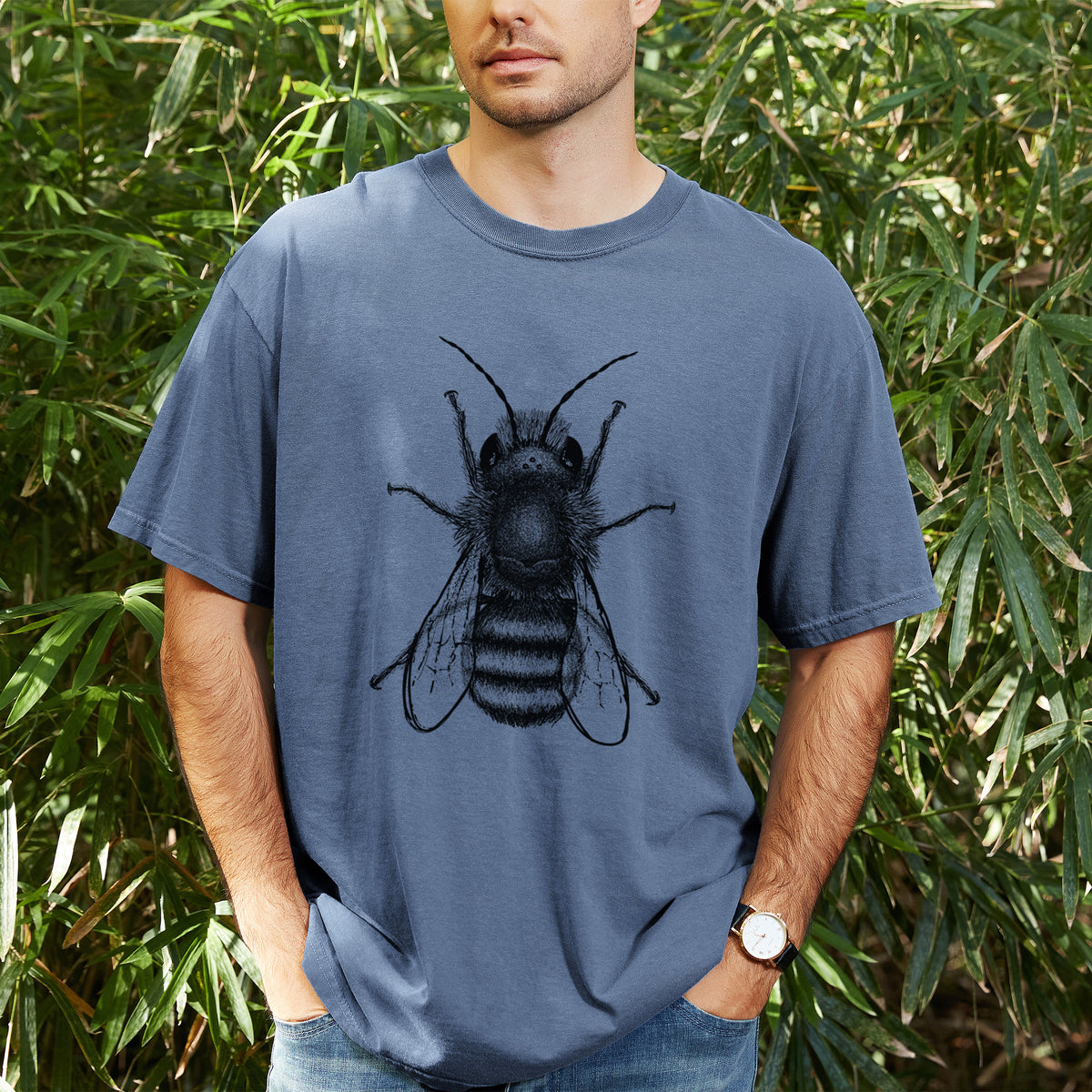 Man wearing a Comfort Colors t-shirt printed with a detailed black ink illustration of a red mason bee with its wings spread, seen from above, outdoors.