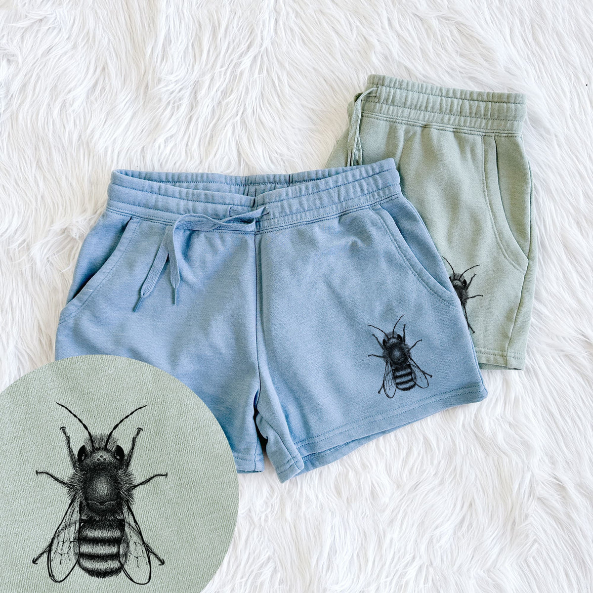 Two pairs of Cali Wave shorts in different colors printed with a detailed black ink illustration of a red mason bee with its wings spread, seen from above, with a close-up of the print.