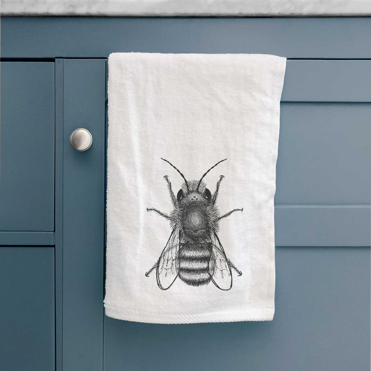 White hand towel printed with a detailed black ink illustration of a red mason bee with its wings spread, seen from above, hanging on a cabinet door.
