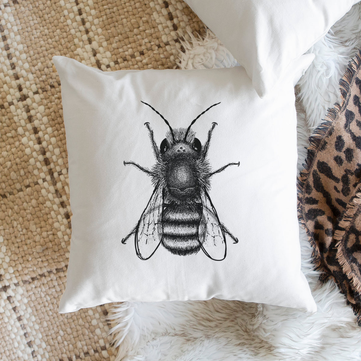 White pillow cover printed with a detailed black ink illustration of a red mason bee with its wings spread, seen from above, on a woven chair.