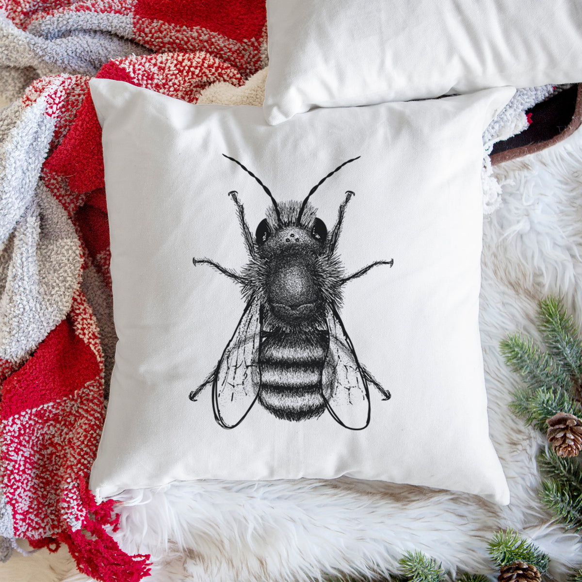 White pillow cover printed with a detailed black ink illustration of a red mason bee with its wings spread, seen from above, on a woven chair.
