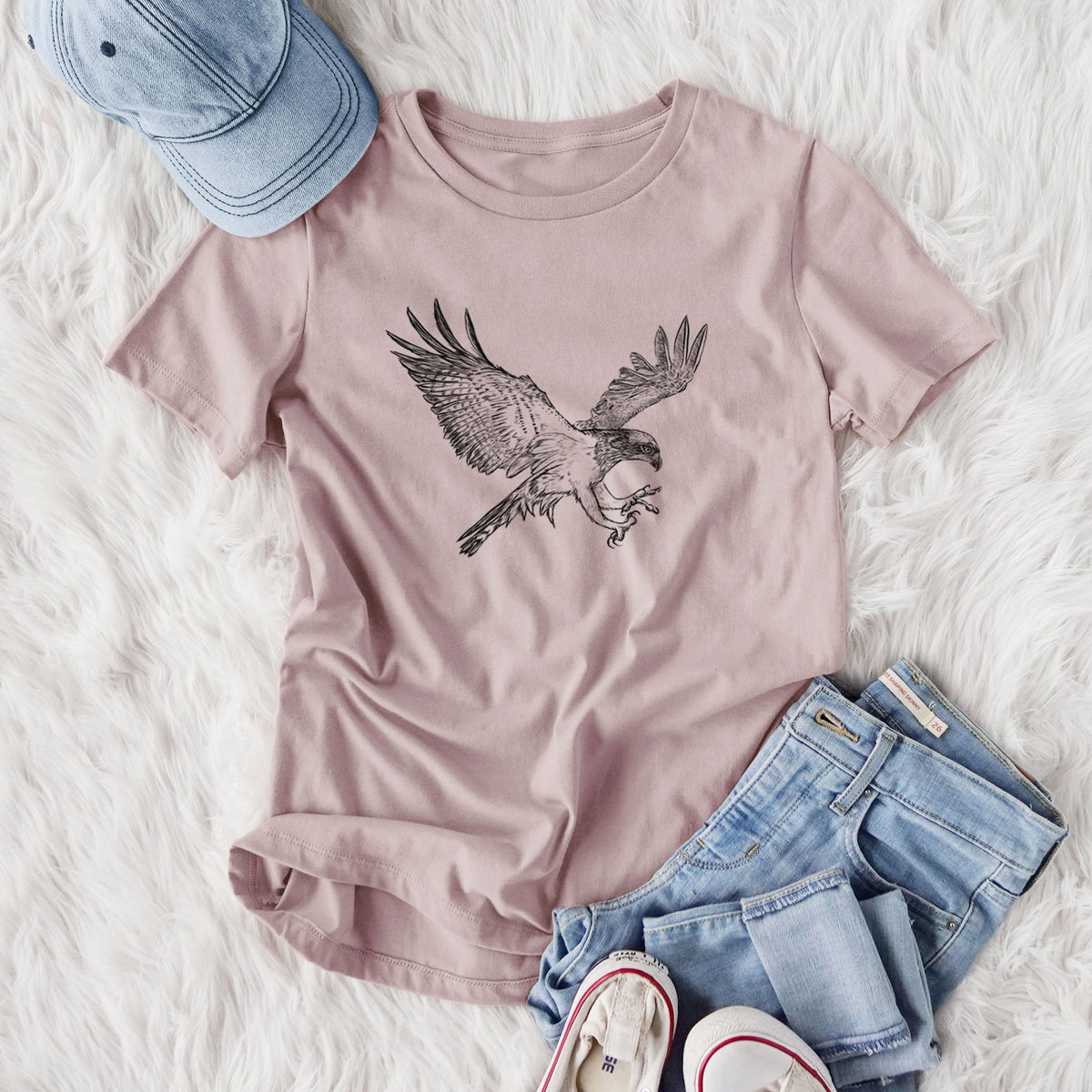 Women's relaxed fit cotton t-shirt printed with a black ink illustration of an osprey in flight with its wings spread, styled flat on a white faux fur rug with jeans.
