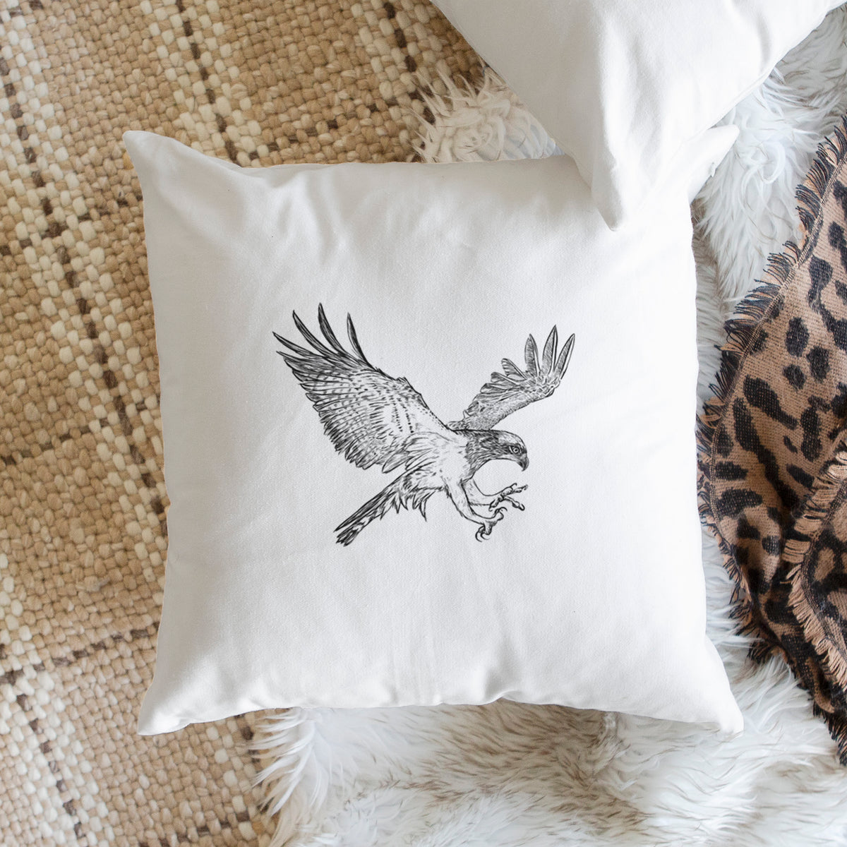 White pillow cover printed with a black ink illustration of an osprey in flight with its wings spread, on a woven chair.