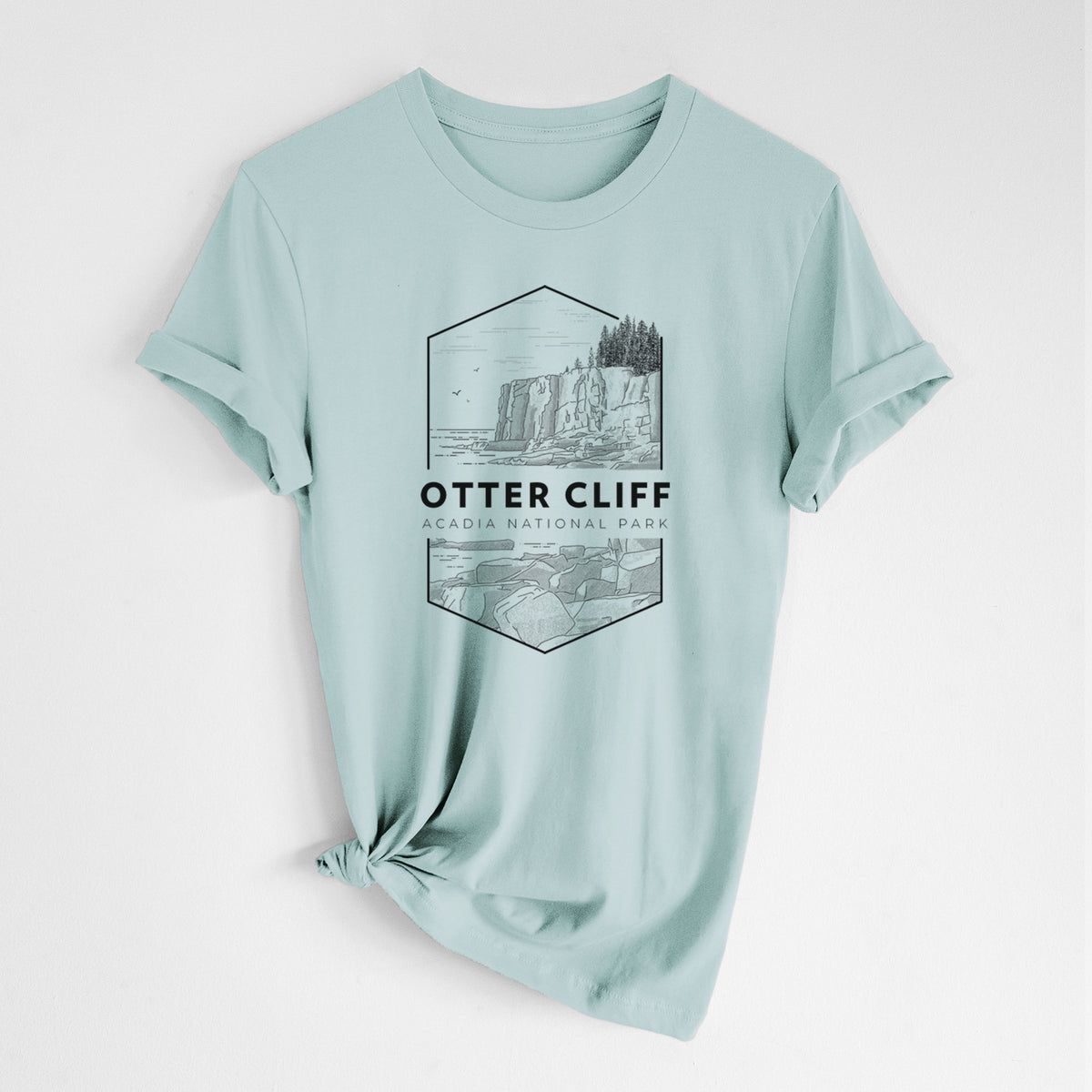 Dusty blue lightweight cotton t-shirt laid flat with the sleeves rolled, printed with a black line art badge of Otter Cliff above the ocean, with the words Otter Cliff, Acadia National Park.