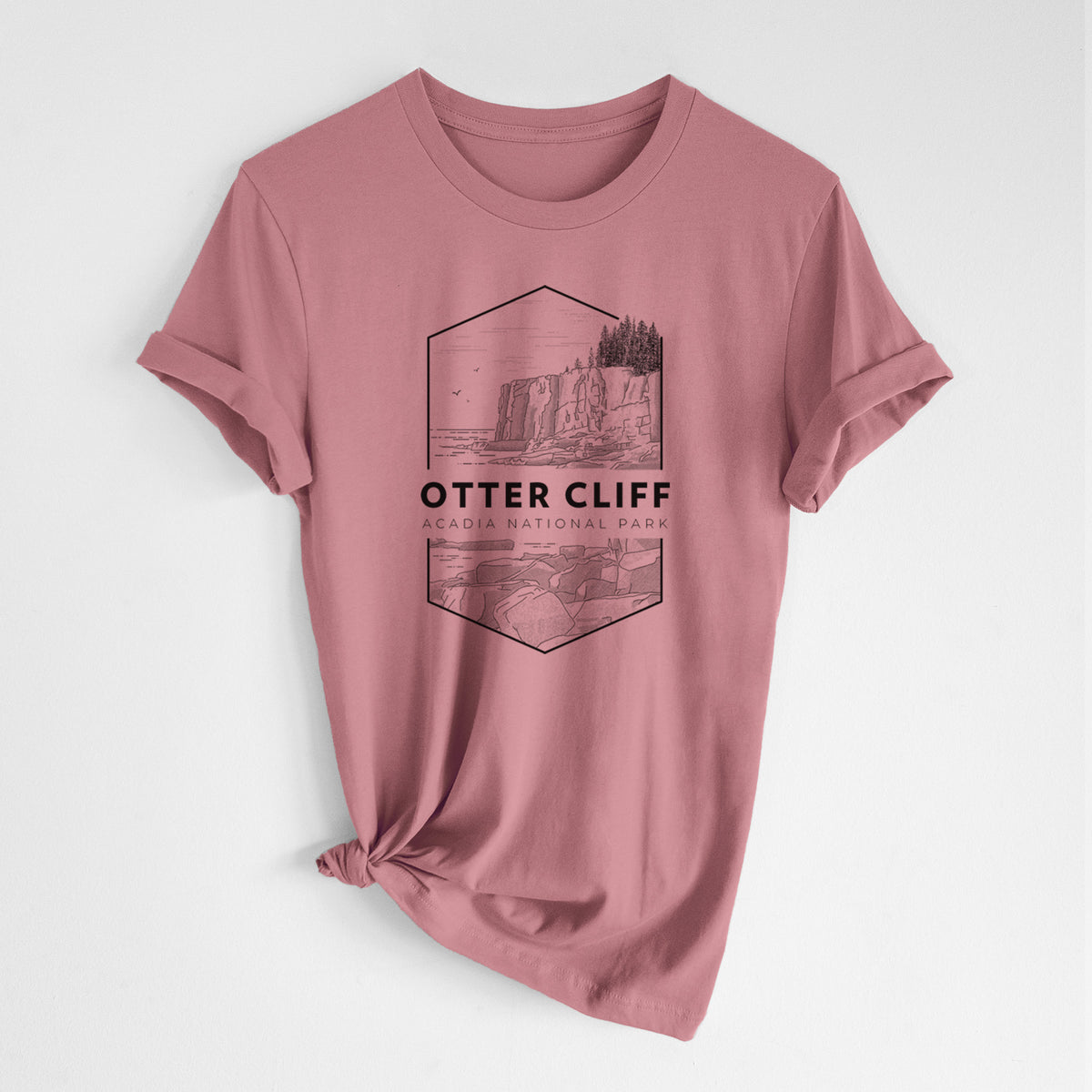 Mauve pink lightweight cotton t-shirt laid flat with the sleeves rolled, printed with a black line art badge of Otter Cliff above the ocean, with the words Otter Cliff, Acadia National Park.