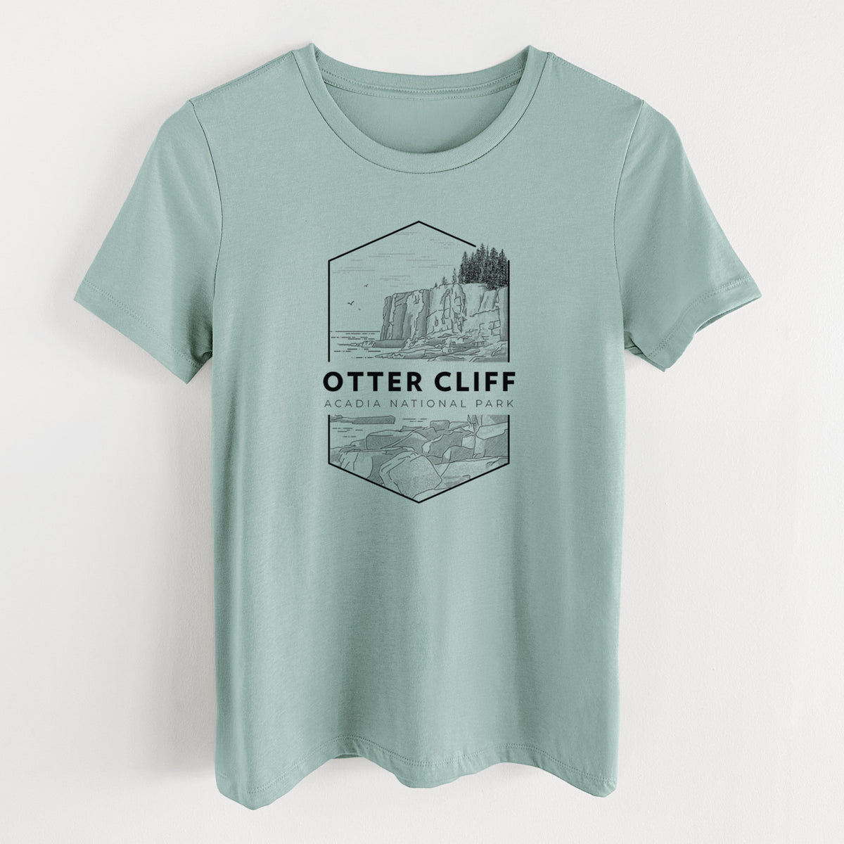 Dusty blue women's relaxed fit cotton t-shirt laid flat, printed with a black line art badge of Otter Cliff above the ocean, with the words Otter Cliff, Acadia National Park.