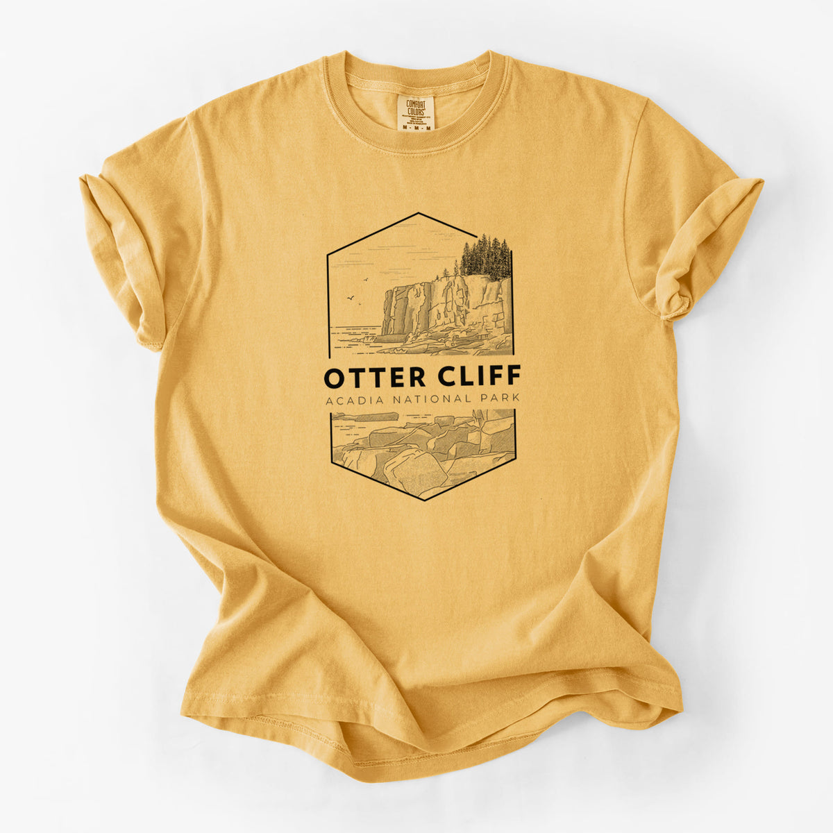 Golden wheat yellow Comfort Colors t-shirt laid flat, printed with a black line art badge of Otter Cliff above the ocean, with the words Otter Cliff, Acadia National Park.
