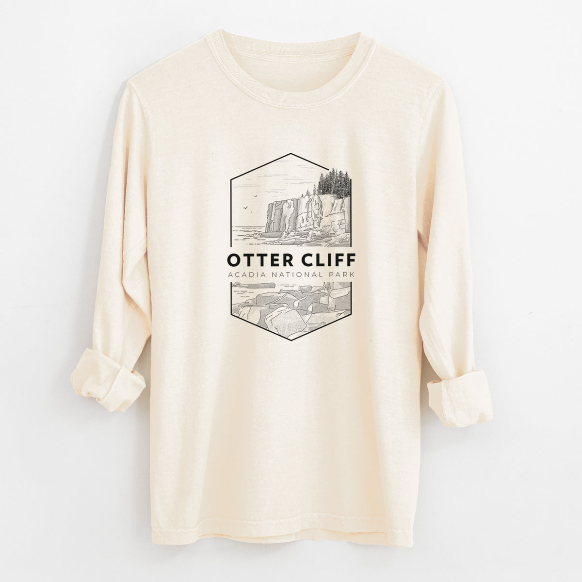 Ivory Comfort Colors long sleeve shirt laid flat with the cuffs rolled, printed with a black line art badge of Otter Cliff above the ocean, with the words Otter Cliff, Acadia National Park.