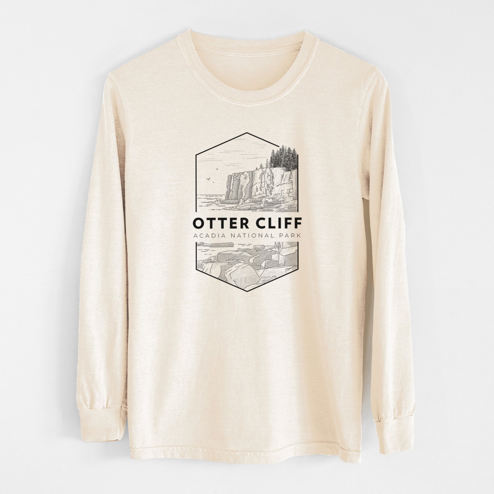 Ivory Comfort Colors long sleeve shirt laid flat, printed with a black line art badge of Otter Cliff above the ocean, with the words Otter Cliff, Acadia National Park.