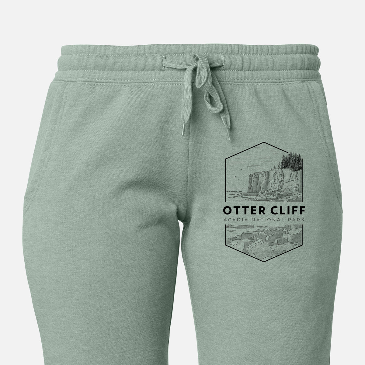 Front of sage green Cali Wave sweatpants, printed with a black line art badge of Otter Cliff above the ocean, with the words Otter Cliff, Acadia National Park on the leg.